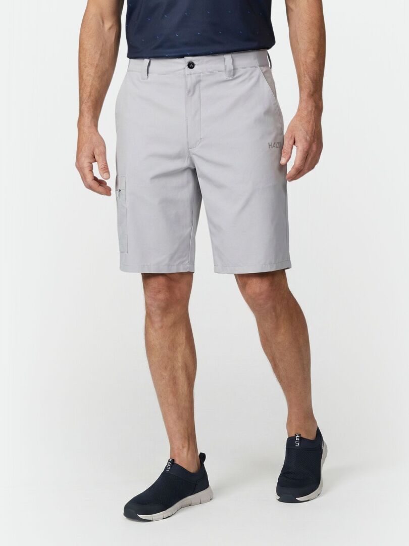 A man wears Halti Drive X-stretch Shorts in light gray, a navy shirt, and slip-on shoes against a white background.