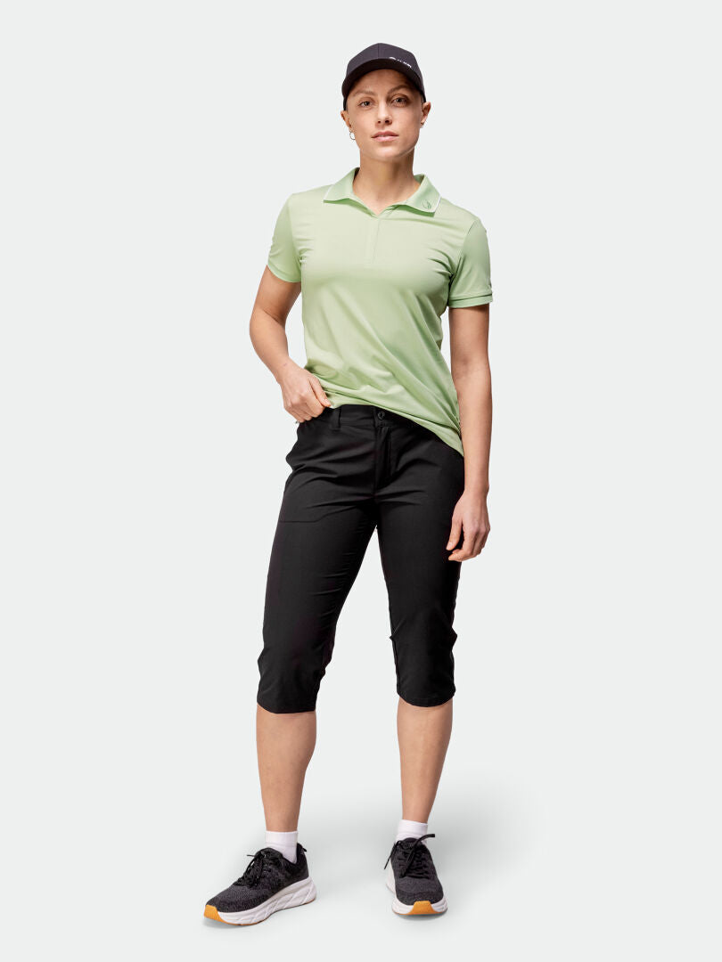 Person wearing Halti Drive X-stretch Capri Pants, light green polo, black cap, and sneakers against a plain background.