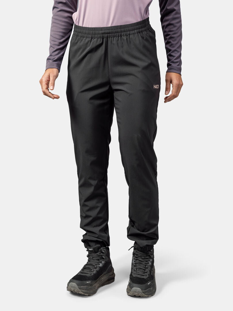 A person in Halti Grets Jogger Pants for women, black hiking shoes, and a mauve shirt stands against a plain background.