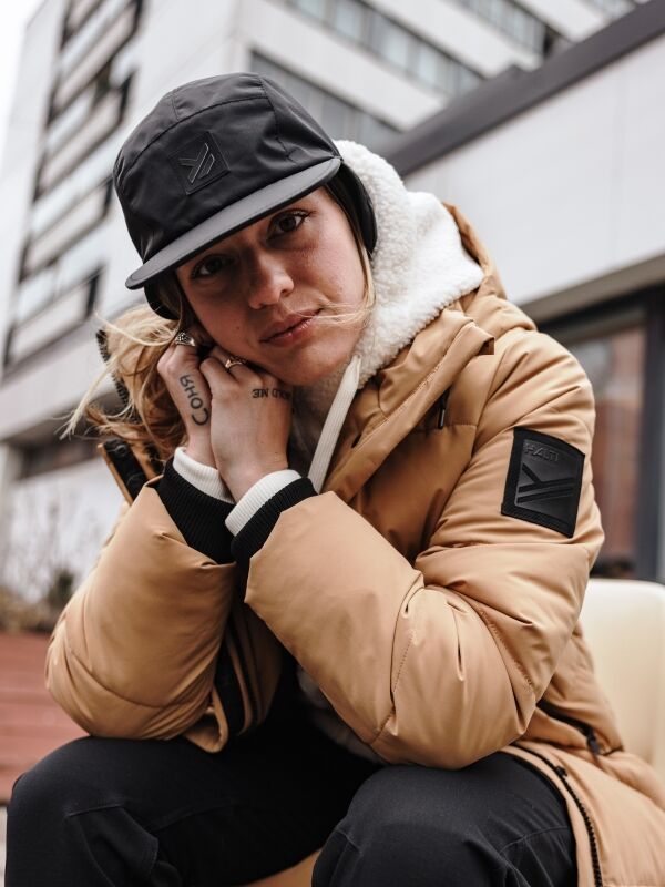 Woman wearing Halti Brahe Puffer Long Winter Jacket and black hat outdoors, cityscape in the background.