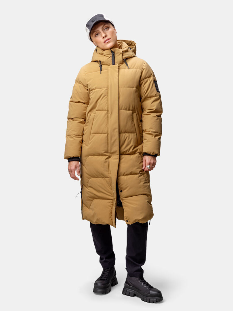 Woman in Halti Brahe Puffer Long Winter Jacket, black pants and boots, gray cap, against a plain background.