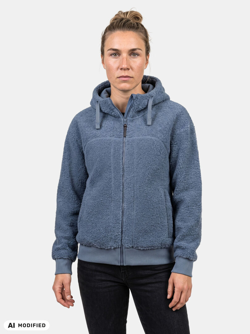 A model faces forward in Halti’s Lykky Fleece Jacket Women’s in blue sherpa, paired with dark pants, plain backdrop.