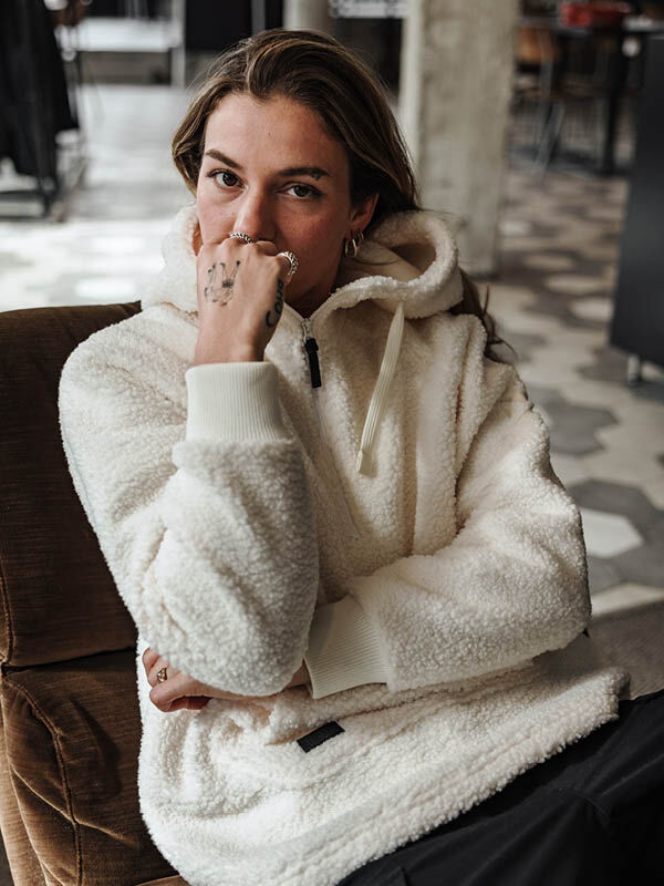 A woman wearing the Halti Lykky Fleece Jacket sits indoors, hand partially covering her mouth.