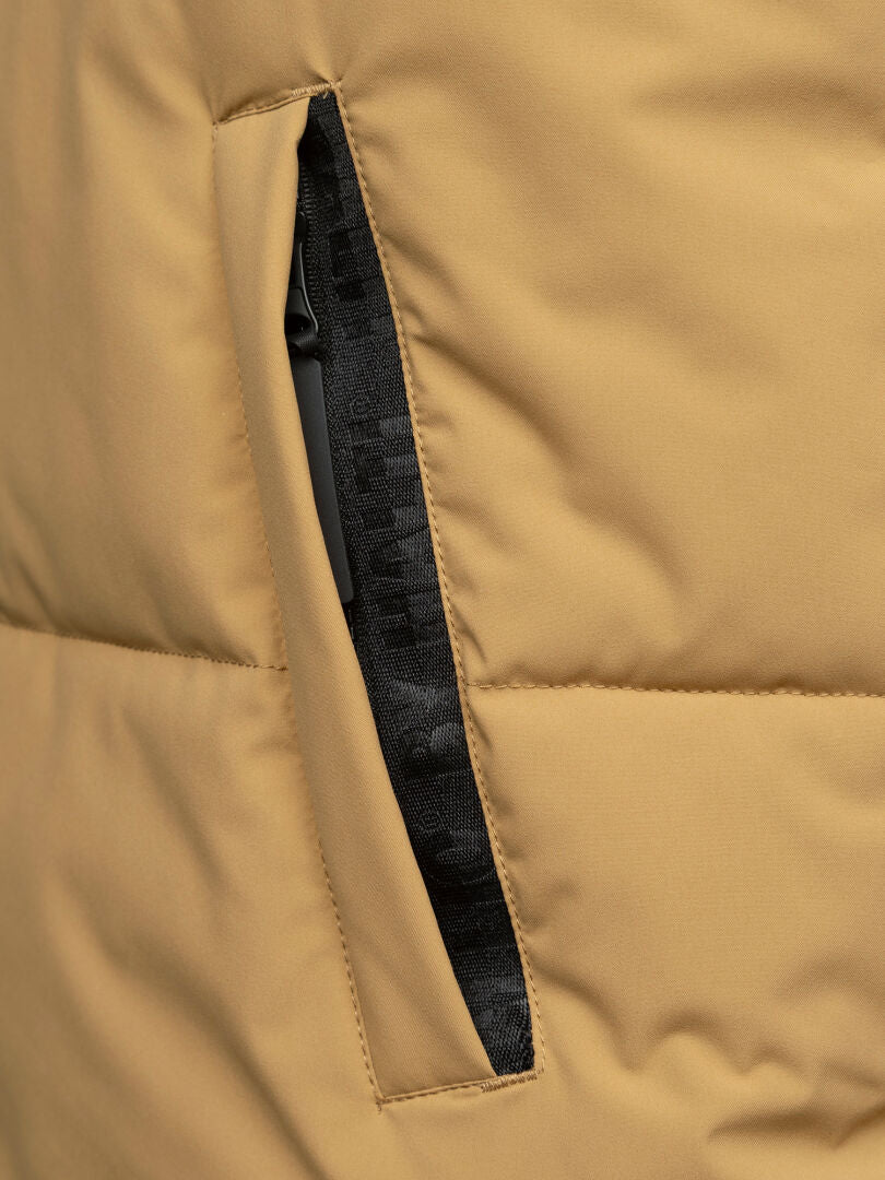 Close-up of the Halti Penger Classic Puffer Vest Men's in tan, featuring a vertical black zipper pocket partially open.