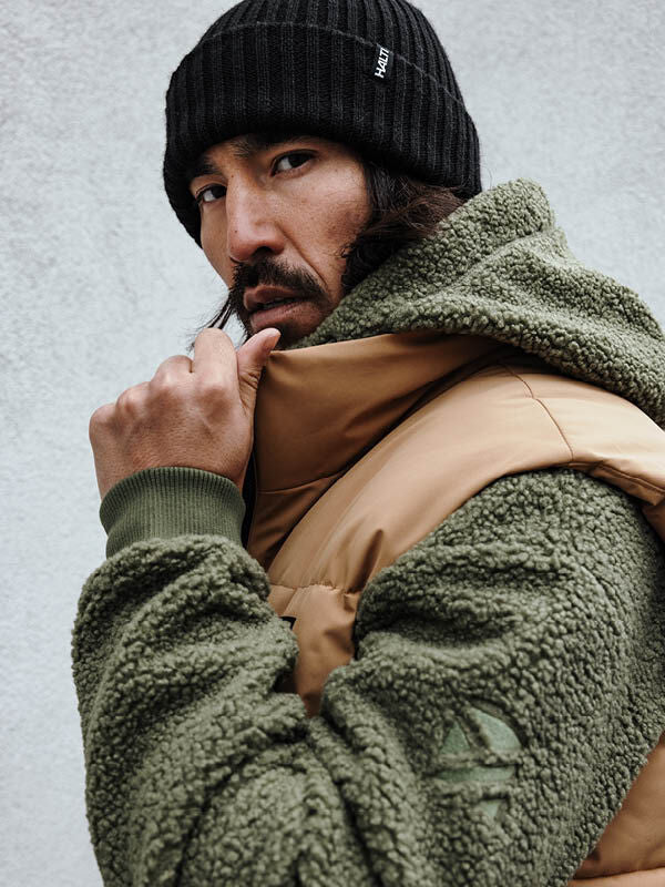 Man in a Halti Runko Beanie and green fleece jacket looks over his shoulder against a plain light background.