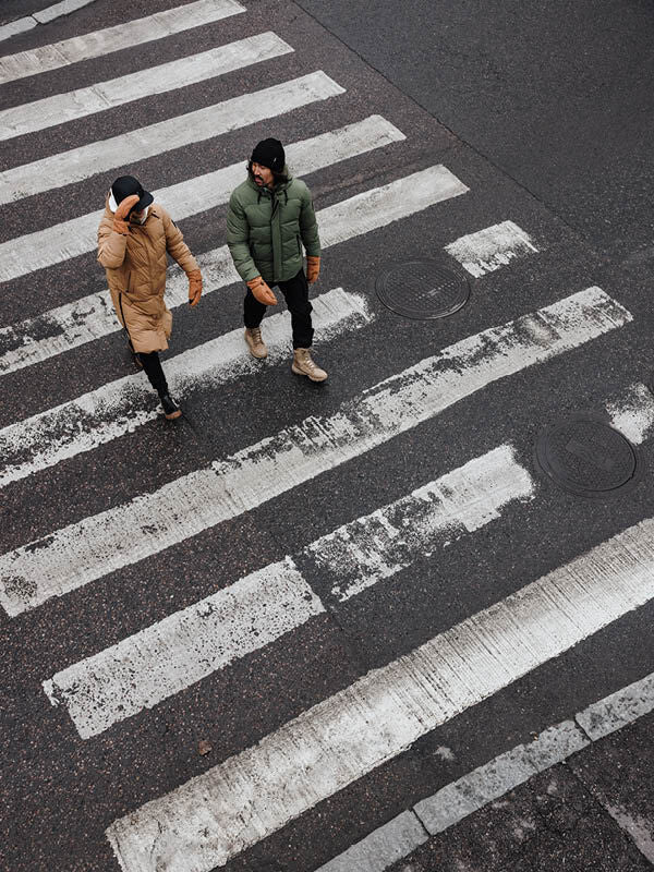 Two men in Halti Brahe Puffer Winter Jackets walk side by side across a city crosswalk on a winter day, seen from above.