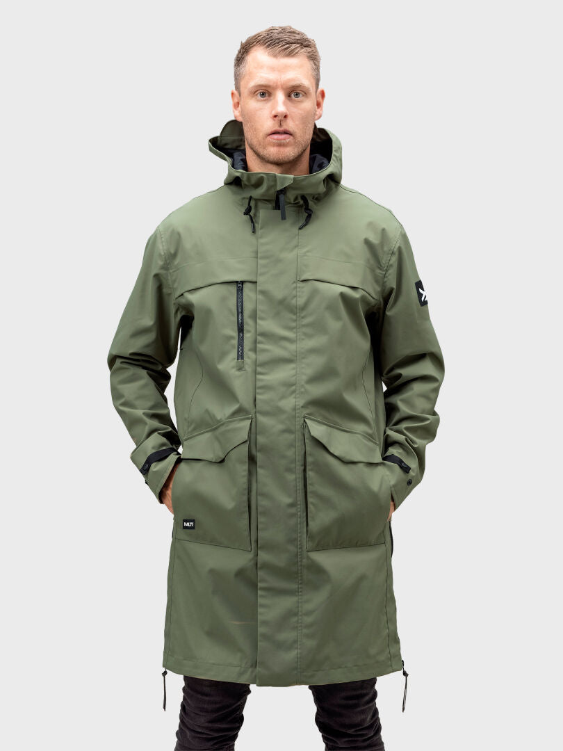 A person models the Halti Tokoi II DX Parka Jacket Men's, olive-green with hood, hands in pockets, on a plain background.