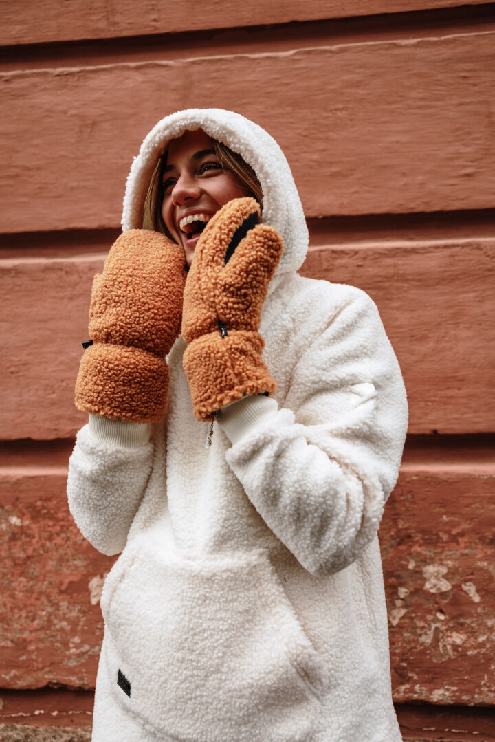 Woman wearing Halti Lykky Fleece Pullover, smiling in front of a textured reddish-brown wall.
