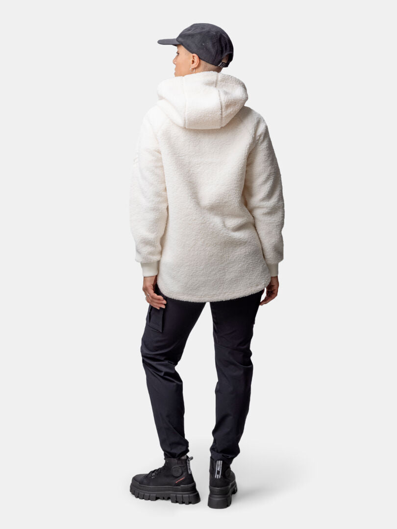 Person stands with back to camera, wearing Halti Lykky Fleece Pullover, black pants, boots, and a dark cap.