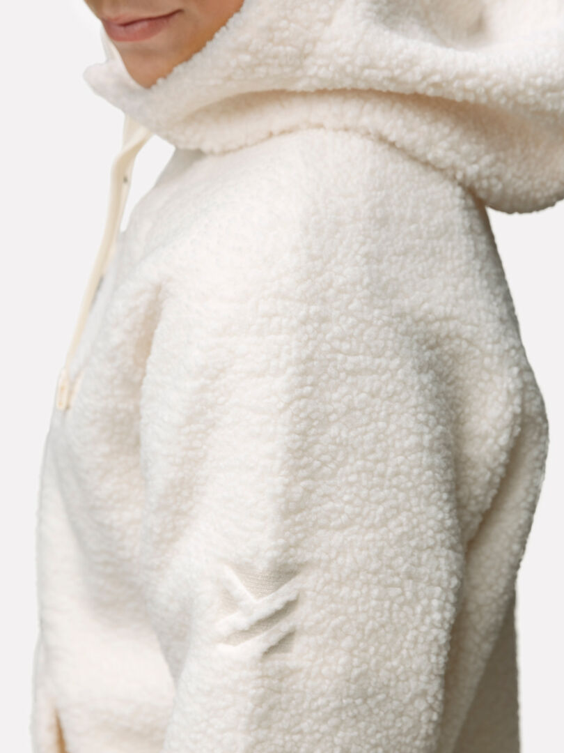 Person wearing Halti Lykky Fleece Pullover Womens—a cream recycled-polyester hoodie with zipper and sleeve logo.