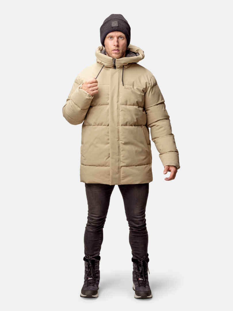 A man wears the Halti Sammal Insulated Parka Jacket with black pants and boots, standing against a plain background.