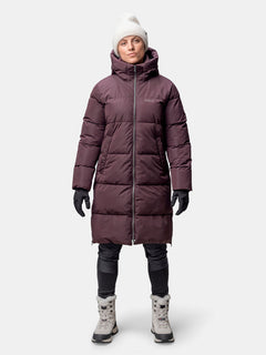A person in a Halti Sammal Insulated Parka Jacket, black gloves, white beanie, black pants, and white winter boots.
