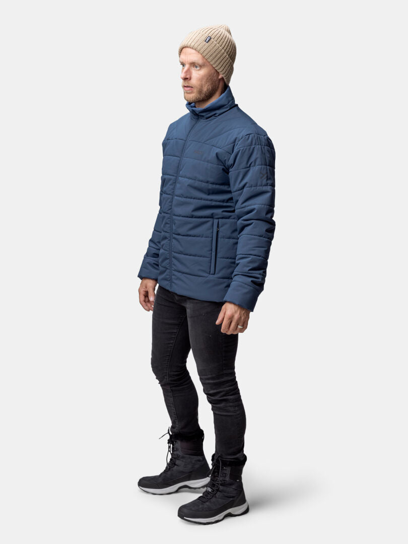A man in a Halti Haapa Insulated Jacket, black jeans, and boots stands against a plain background.