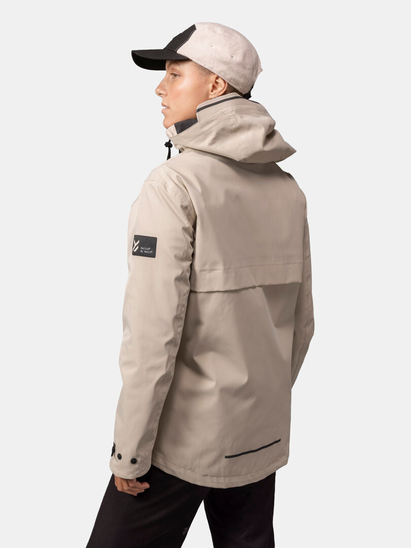 A woman in a beige Halti Tokoi DX Jacket stands sideways against a plain light background, wearing a black-and-white cap.