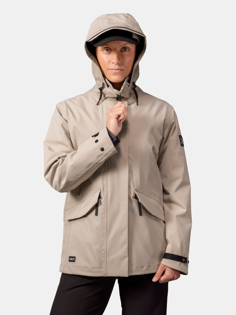 A woman in a beige Halti Tokoi DX Jacket stands forward, holding the weatherproof jacket’s zipper.