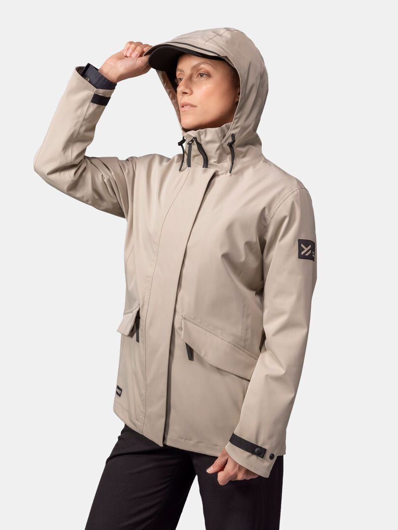 A person in a beige Halti Tokoi DX Jacket for women and black pants stands holding the hood's brim.