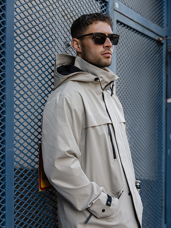 Man in Halti Tokoi DX Jacket and sunglasses stands outdoors against a blue metal fence.