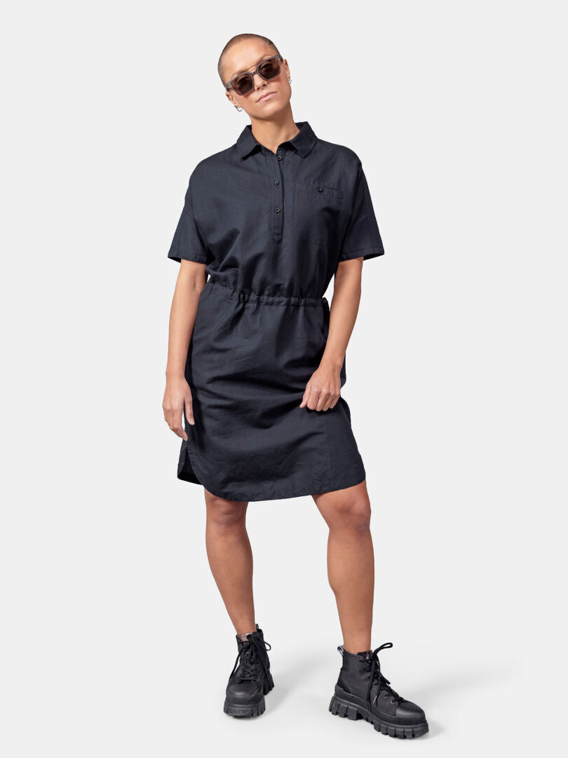 A woman in Halti's Notsgi Dress and lace-up boots stands against a plain background, wearing sunglasses.