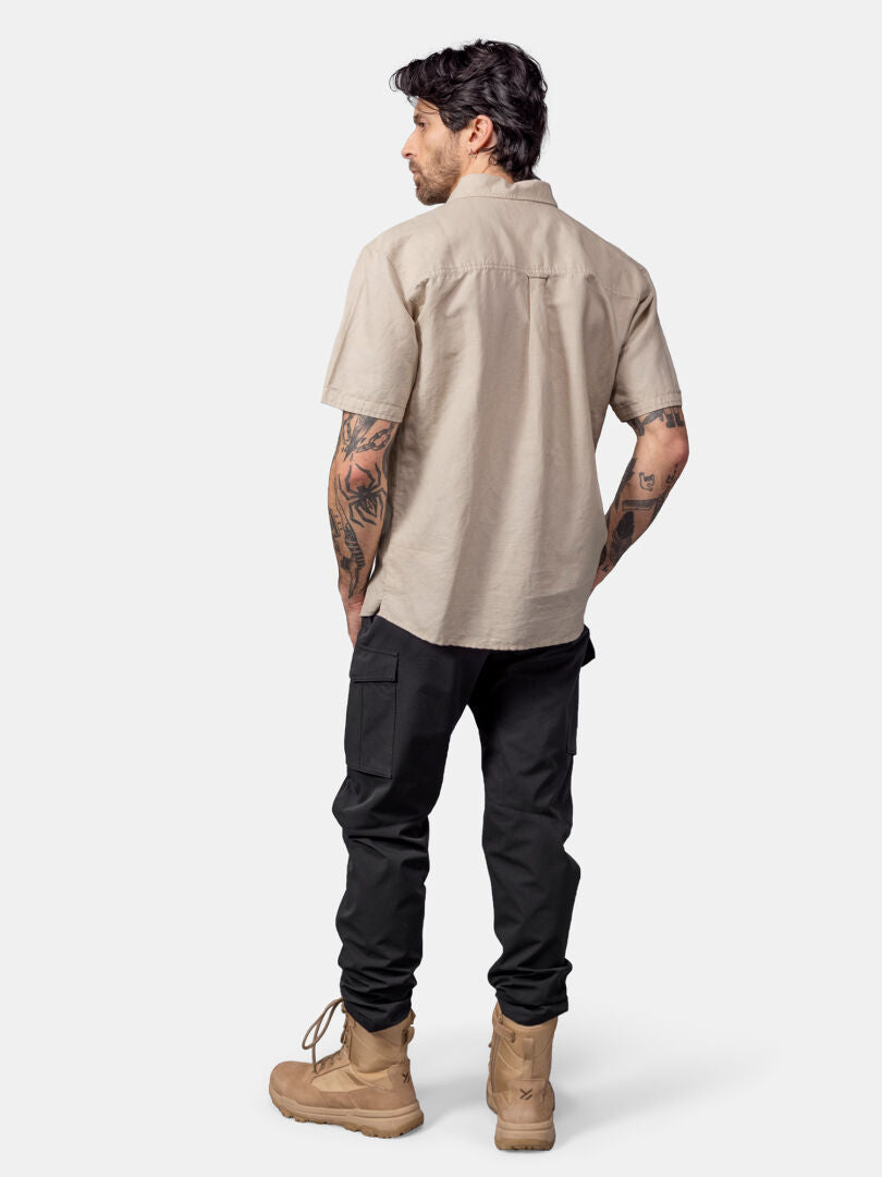 A man faces away, wearing the Halti Notsgi Shirt Men's in beige with black pants and tan boots against a plain background.