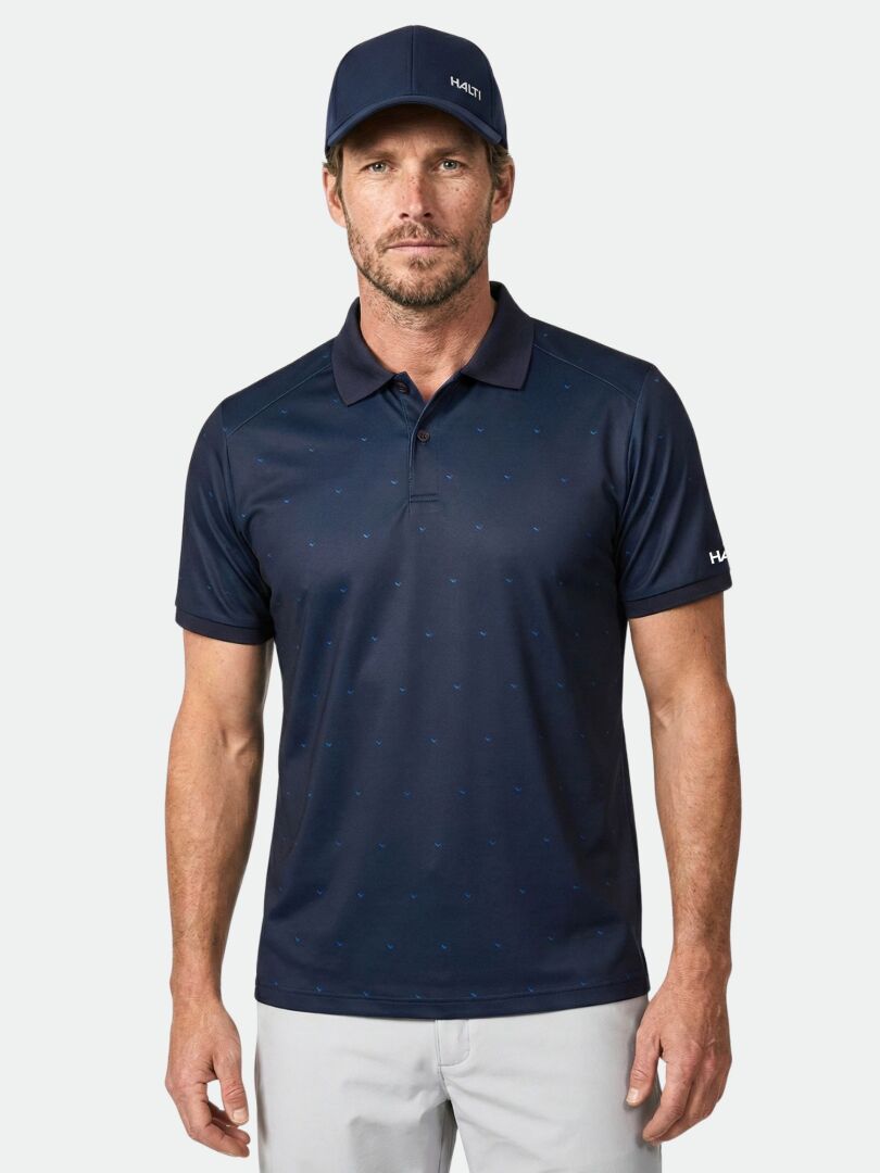 Man in Halti Aridi Technical Polo Shirt and light gray pants with a navy cap, standing against a plain background.