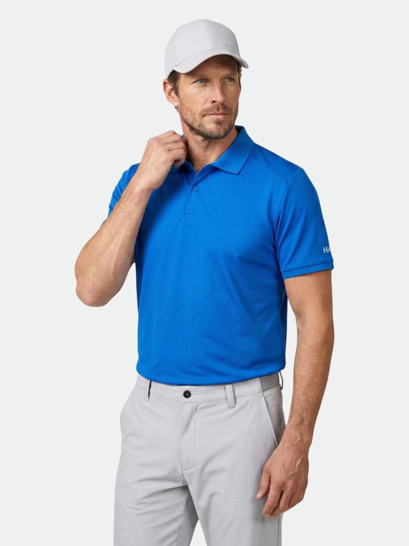 Man wearing the Halti Aridi Technical Polo Shirt, light gray pants, and a white cap against a plain light background.