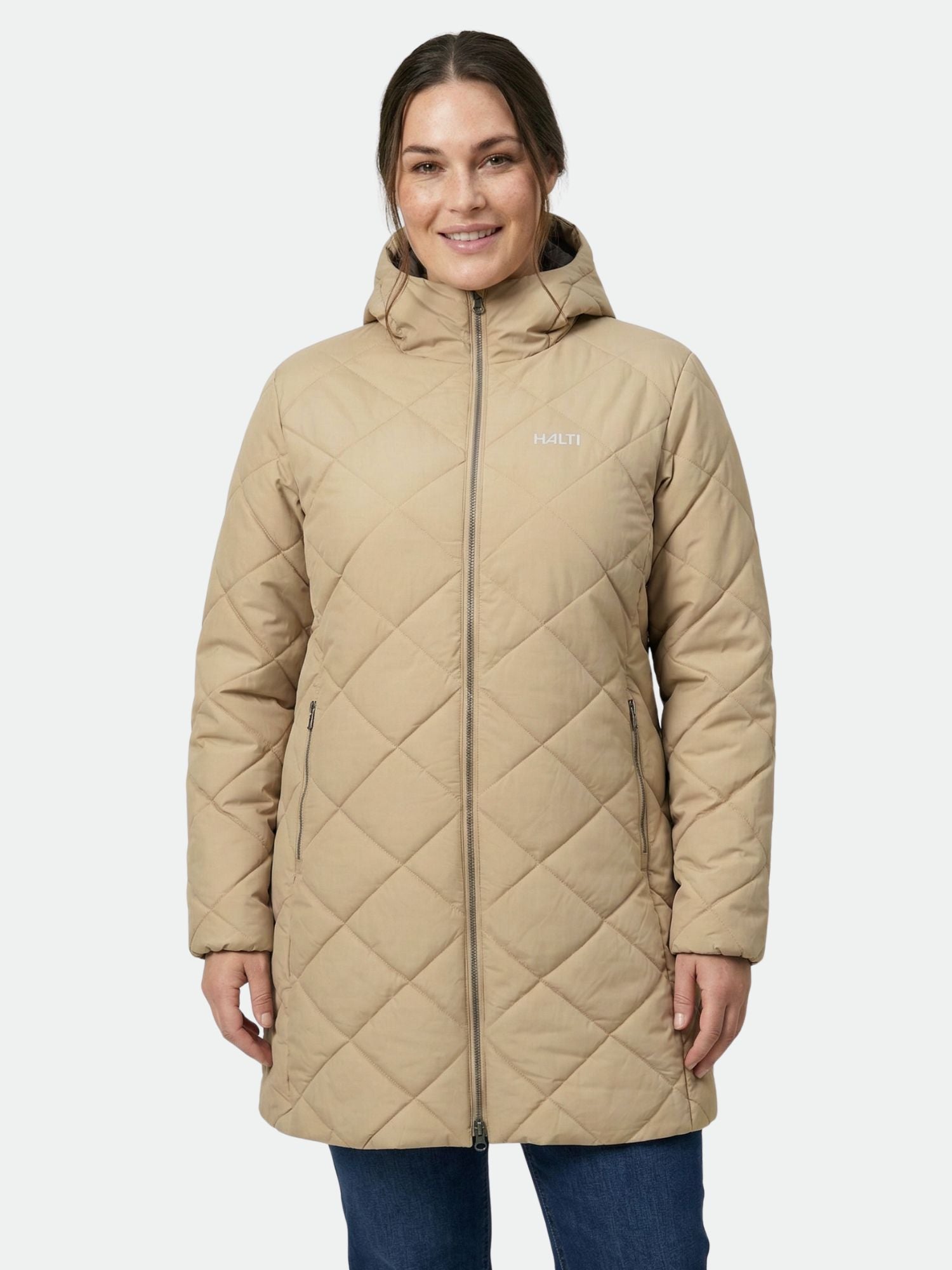 A woman wears the Halti Haapa Quilted Coat Jacket Women's Plus in tan, smiling with hands relaxed at her sides.