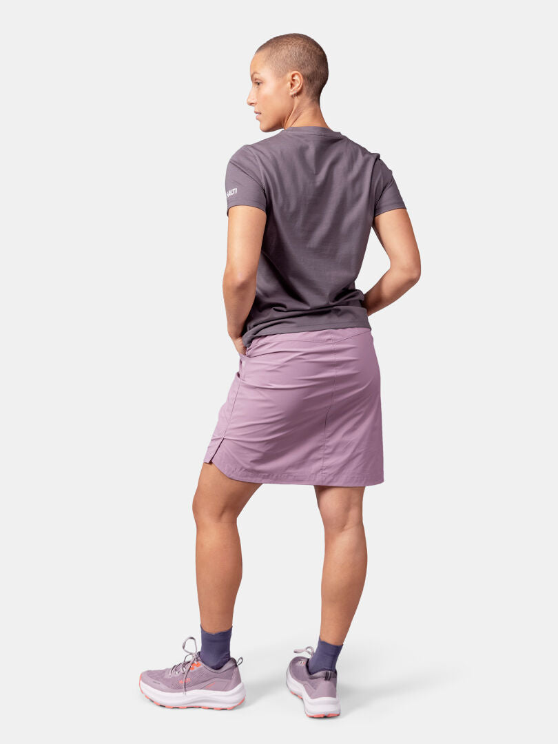 A person faces away, wearing Halti's Matka II T-shirt Women's in grey, with a mauve skirt, socks, and sneakers.
