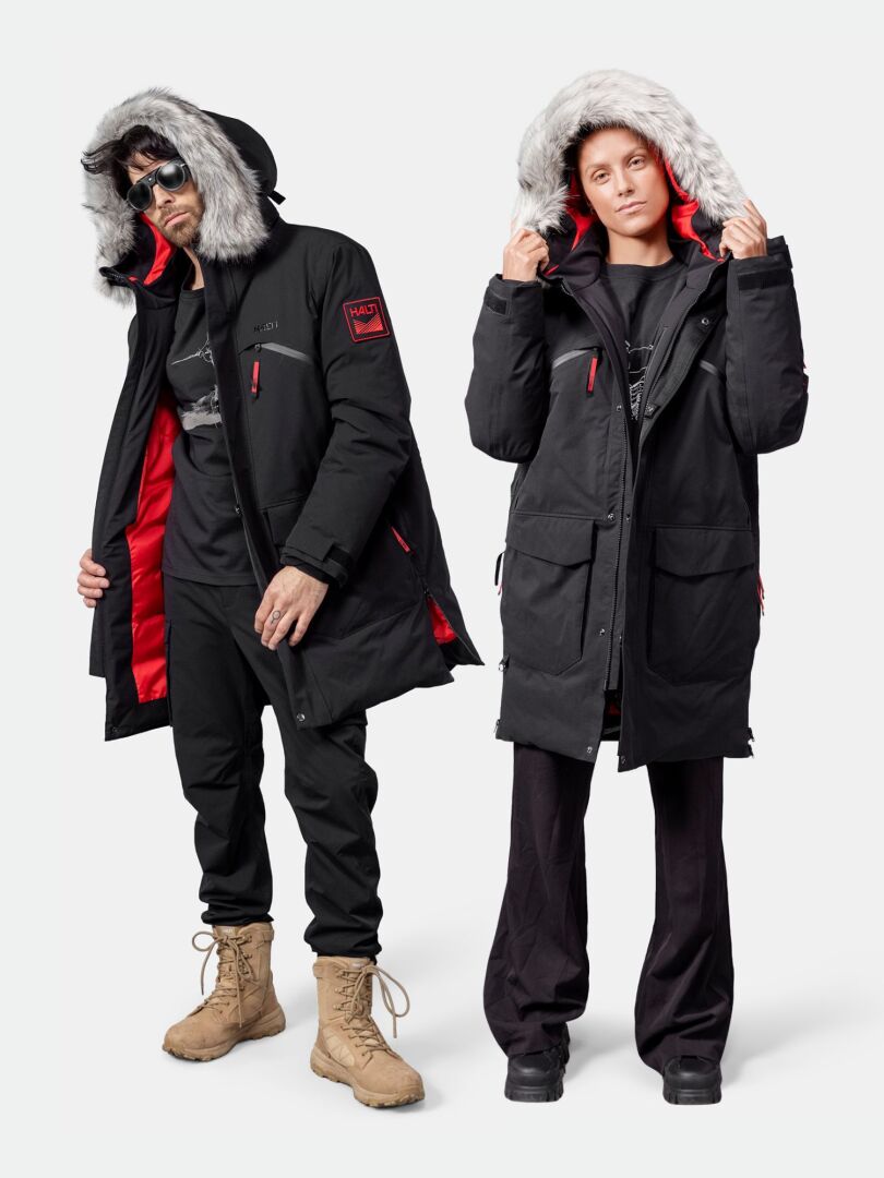 Two people in Halti 1976 Down Parka Unisex, black with fur-lined hoods and red lining, stand against a white background.