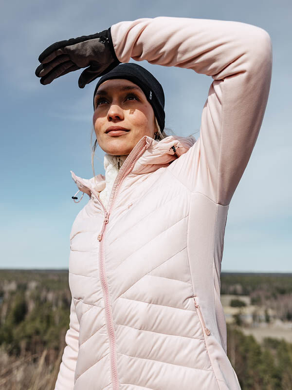 Wearing the Halti Huippu Hybrid Down Jacket, a woman in black gloves shades her eyes outdoors on a clear day.