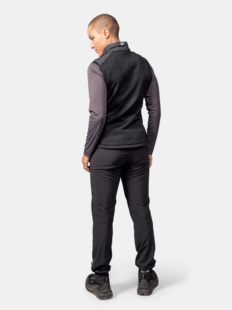 Person stands facing away, wearing Halti Huippu Hybrid Down Vest Women's in black, gray shirt, and black pants.