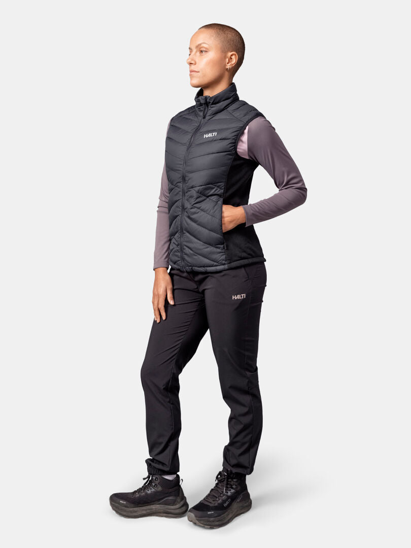 Model wears the Halti Huippu Hybrid Down Vest Women's in black, plus a mauve long-sleeve, black pants, and boots.