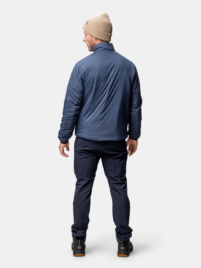 A man in a blue Halti Haave Insulation Primaloft Jacket stands facing away, paired with dark pants.