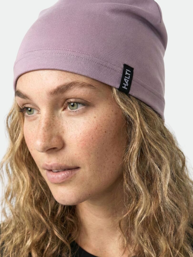 A person with wavy blonde hair wears a light purple Halti Loiva Beanie featuring a black Halti tag.