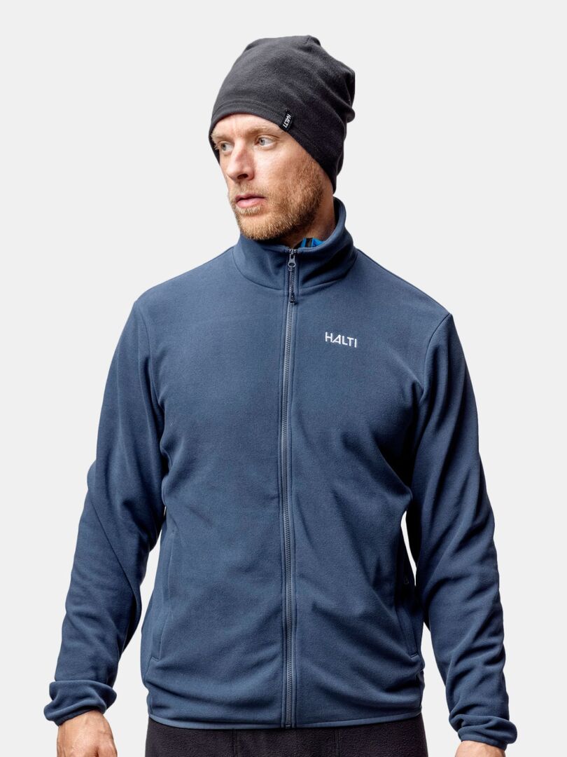 A man wears a Halti Trone Fleece Beanie and a navy blue Halti jacket, standing against a plain background.