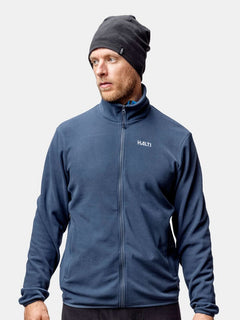 A man wears a Halti Trone Fleece Beanie and a navy blue Halti jacket, standing against a plain background.