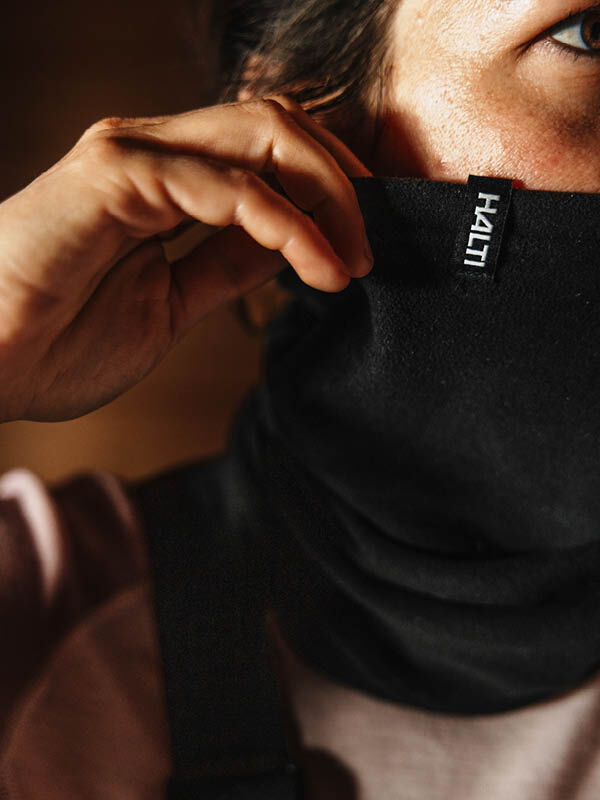 A person adjusts a lightweight Halti Trone Tube Scarf Fleece, which provides thermal insulation over their nose and mouth.