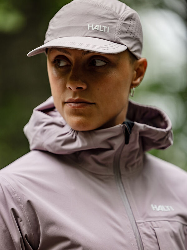 Wearing a light purple jacket and Luovi Cap by Halti, person looks to the side outdoors.