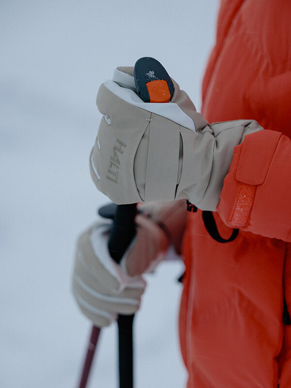 A person in a red jacket wears Halti Vuotos Ski Gloves while holding a ski pole outdoors in the snow.