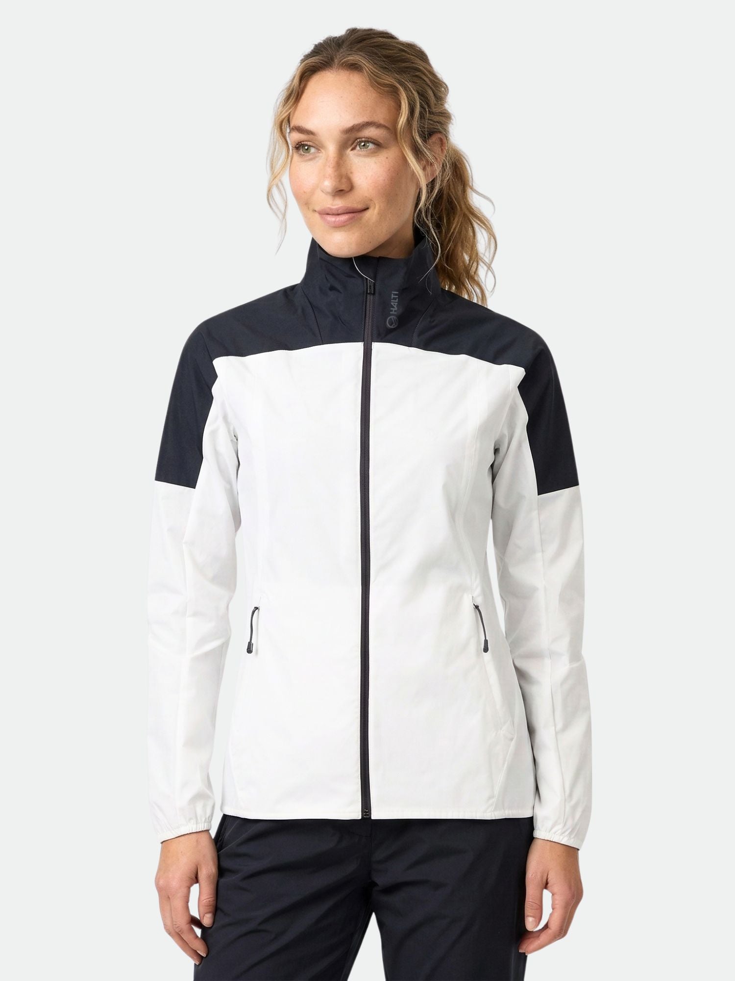 A woman faces forward in a Halti Urbanite Women's Training Jacket and black pants against a plain background.