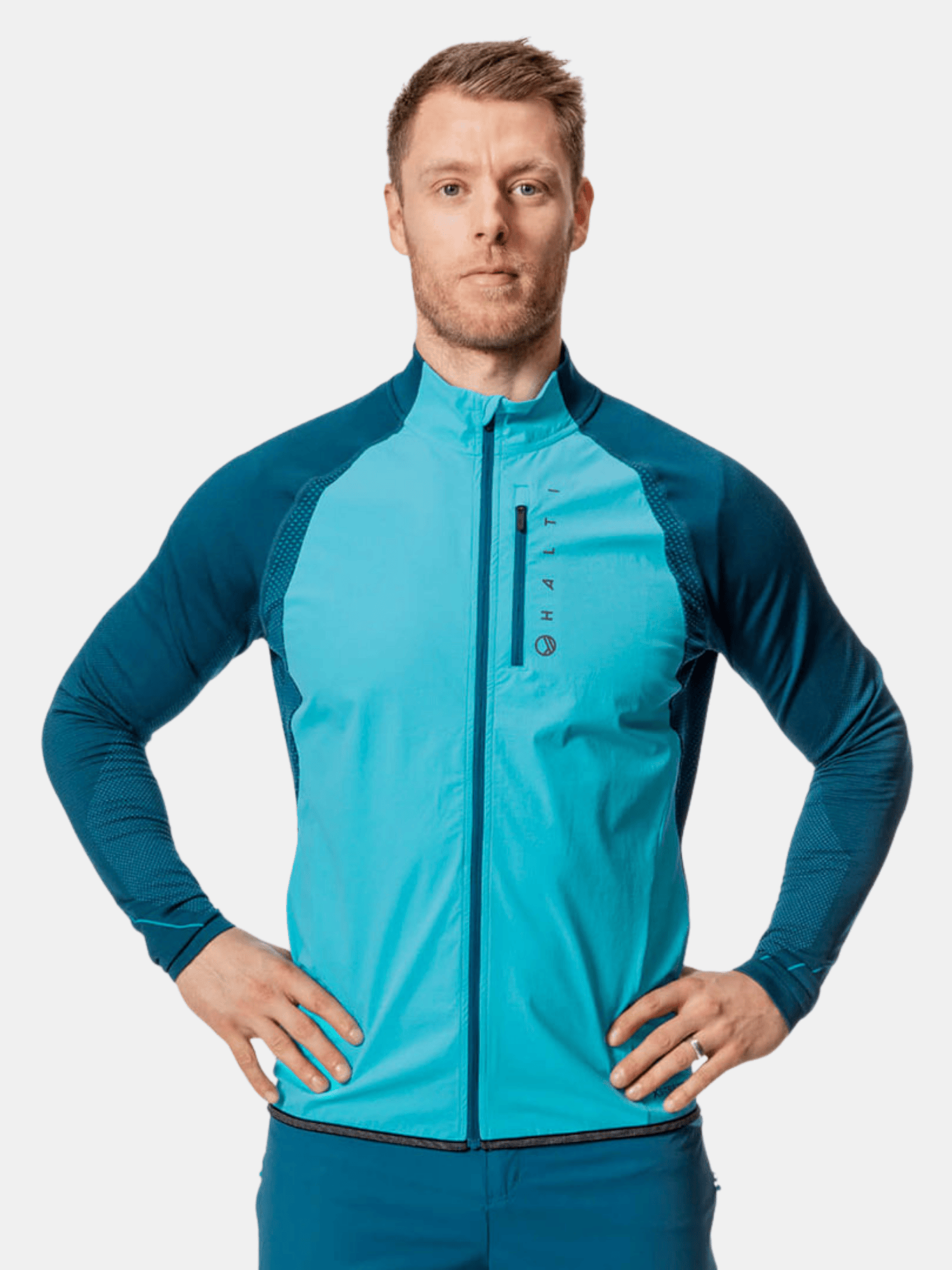 A man in a Halti Tracks Mens Seamless Jacket stands hands on hips, ready for outdoor workouts against a plain background.