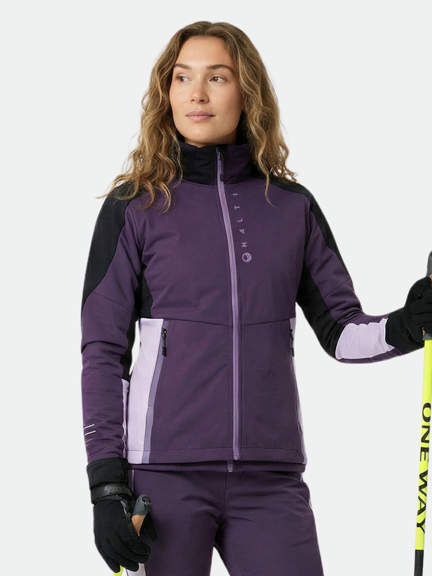 A woman in a Halti Veloce XCT Jacket holds ski poles, looking to the side against a plain background.