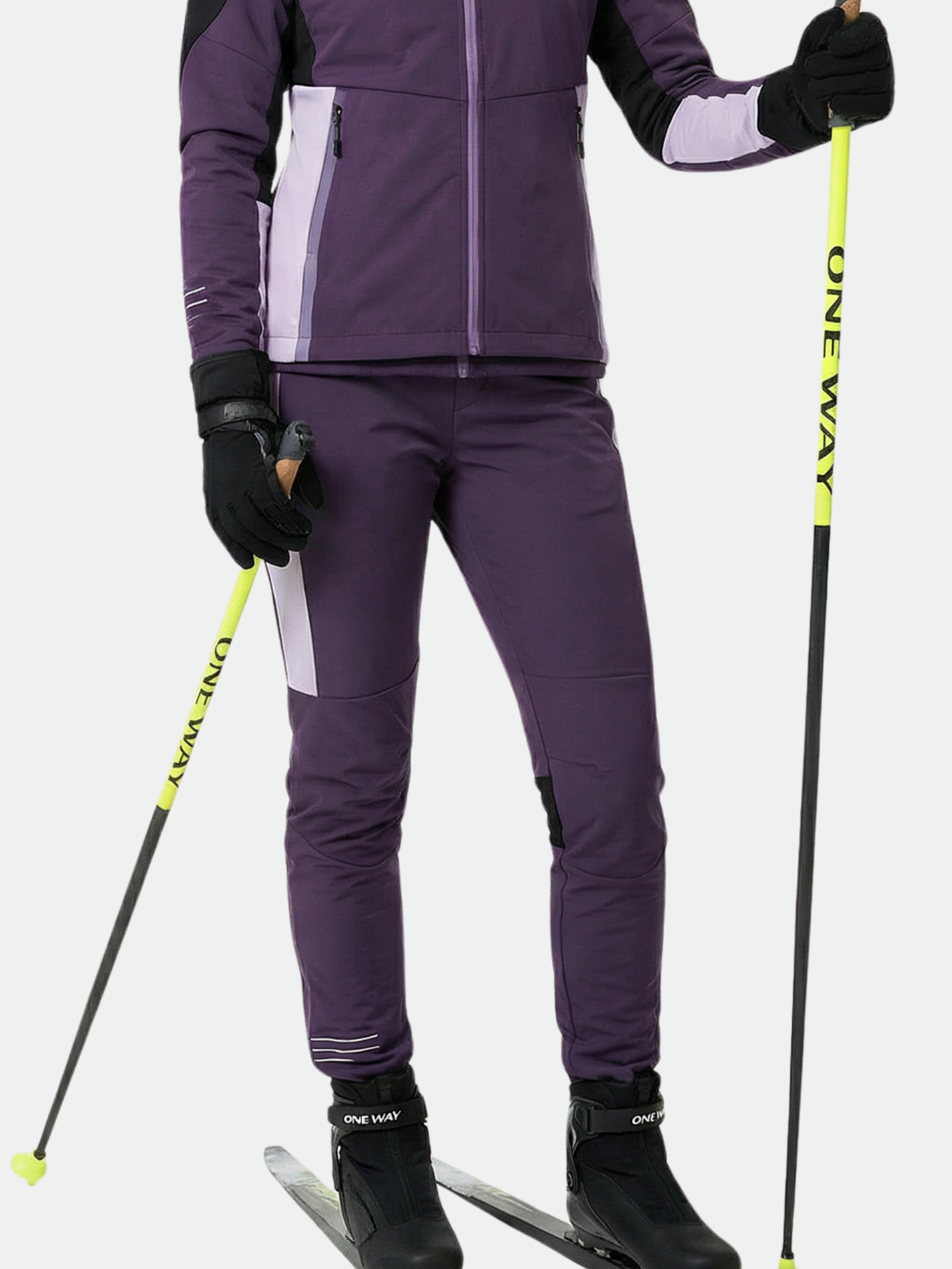 Woman wears Halti Veloce XCT Pants and black gloves, holding yellow ski poles while standing on skis against white background.