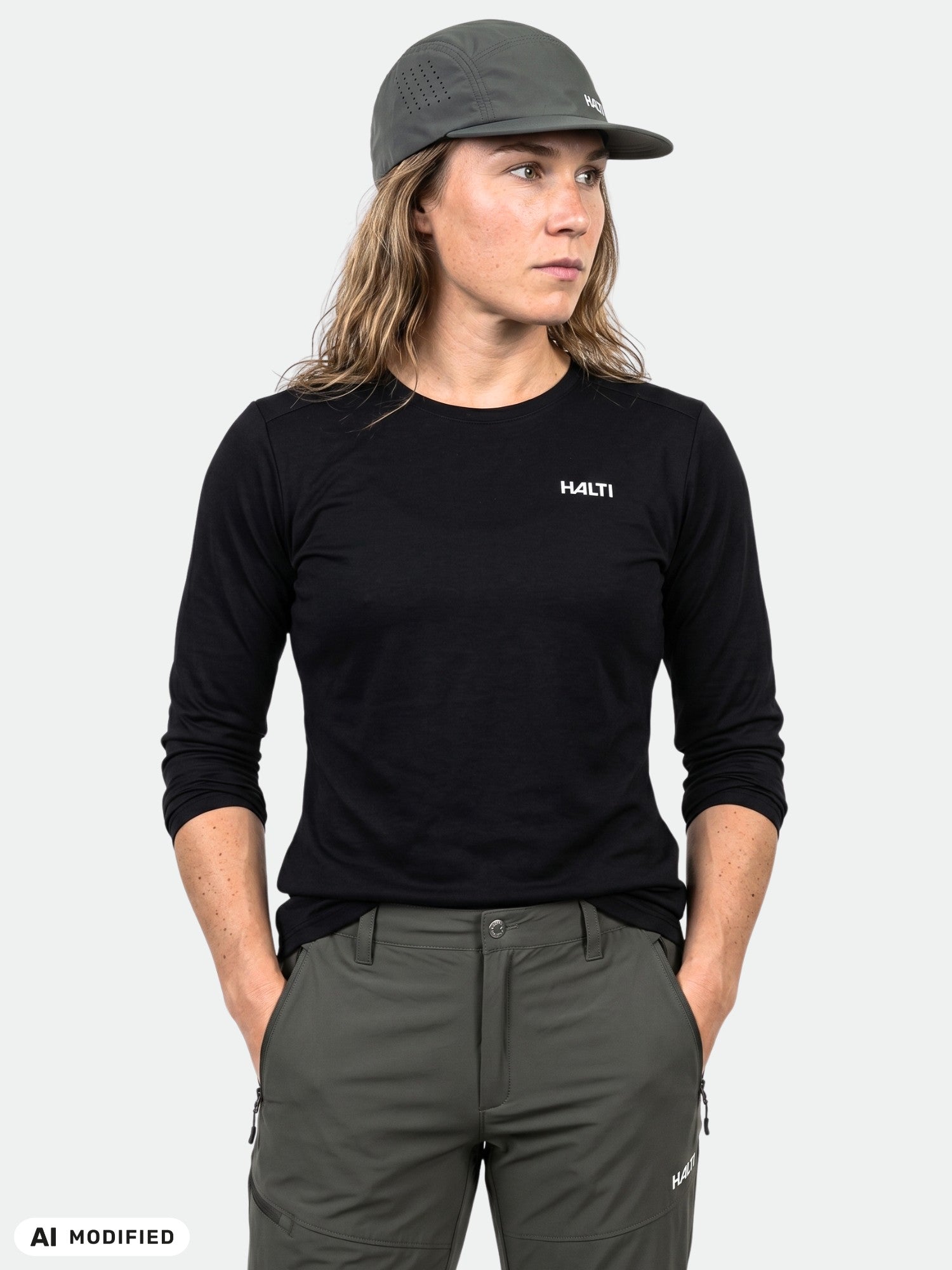 Woman in Halti Salves Training Shirt, olive pants, and cap stands against a plain background.