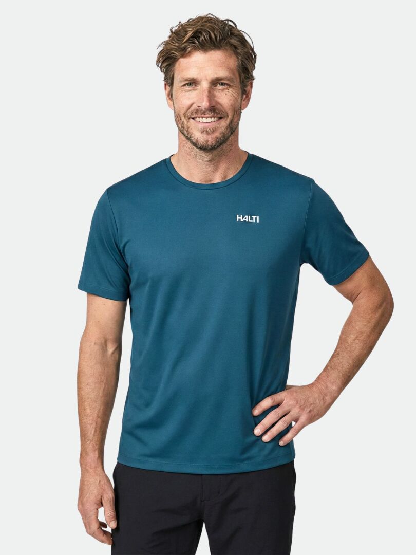 Man smiling in a Halti Salves T-shirt Men's (teal, recycled polyester), styled with black pants against a light background.