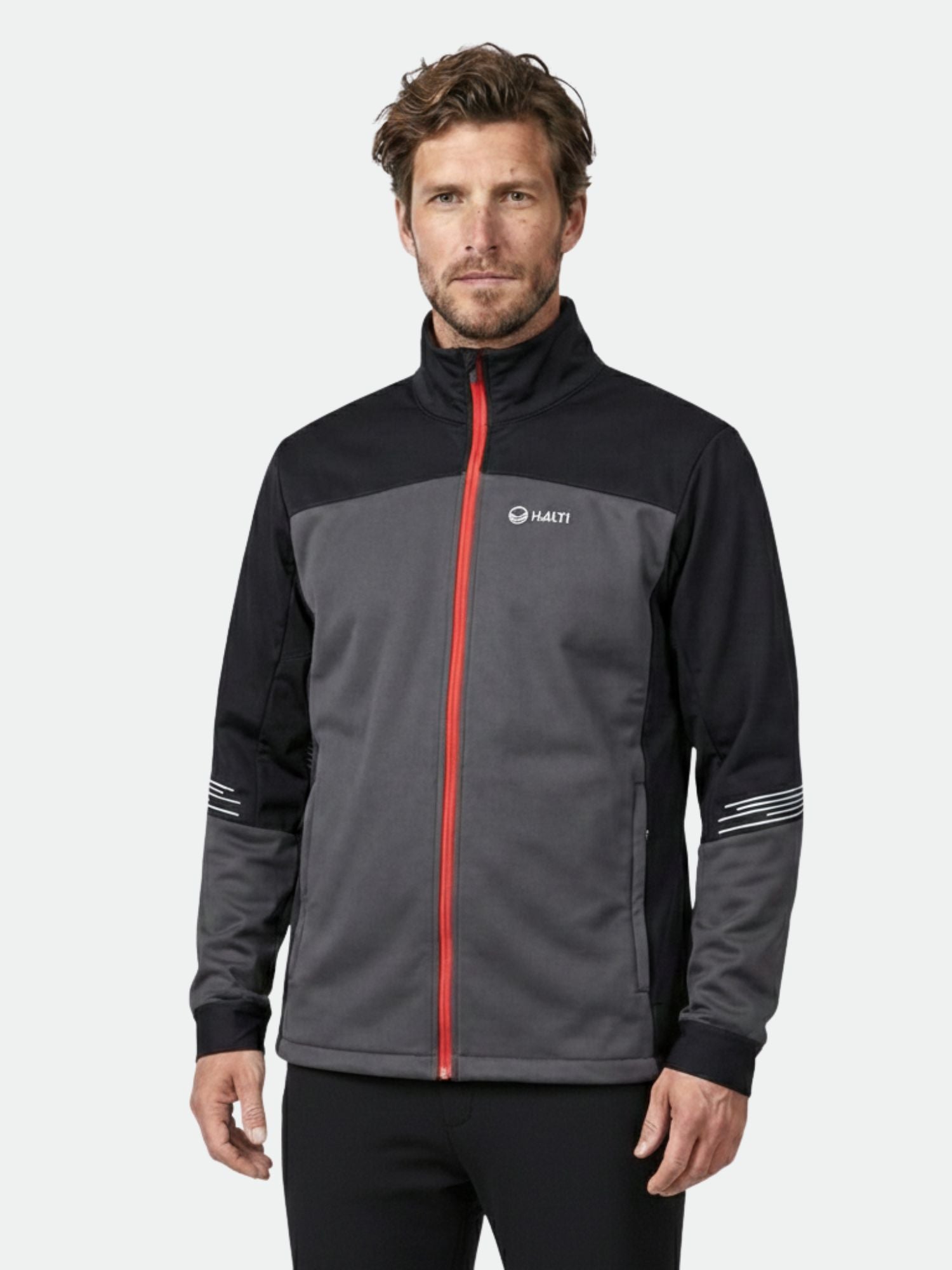 A man wears the Halti Siide XCT Set Men's black and gray windproof zip-up jacket with red zipper, against a plain background.
