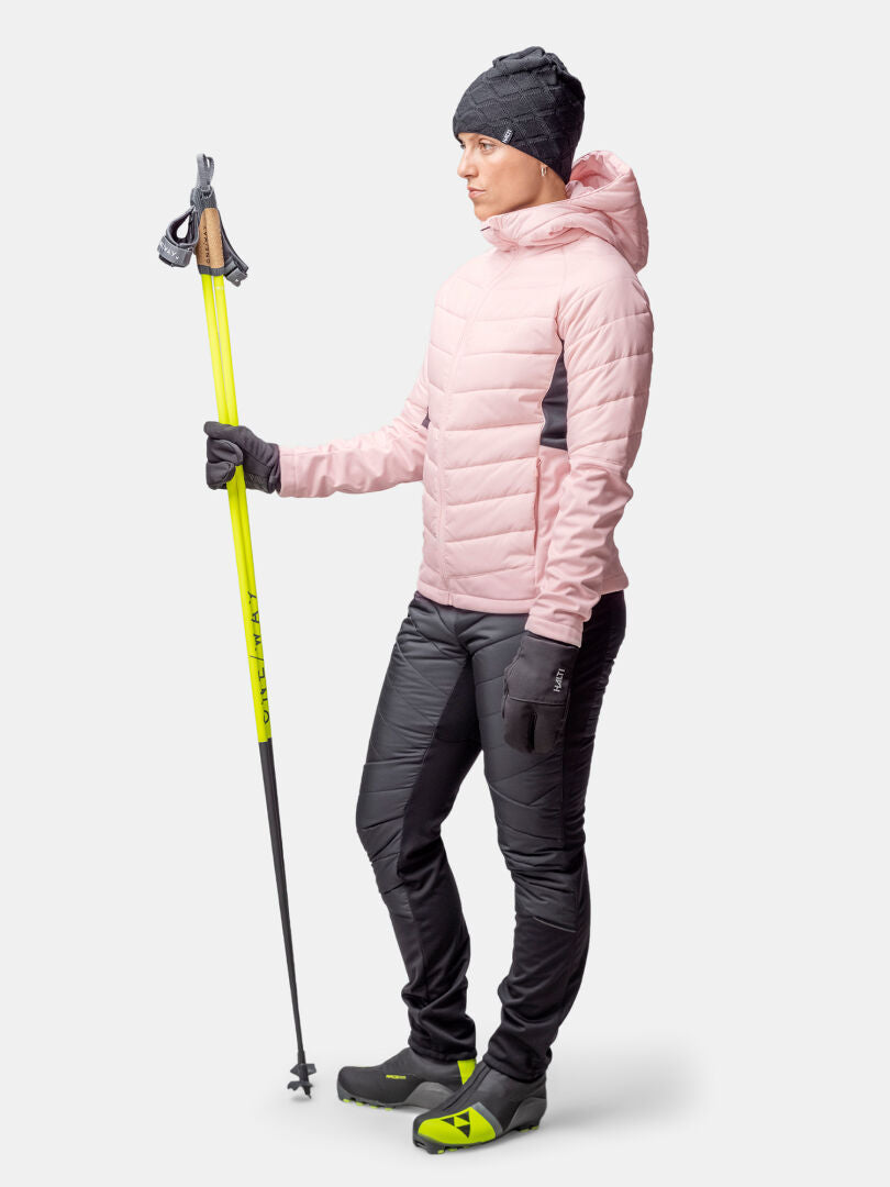 Woman wearing Halti Hanki 2 Hybrid XCT Jacket holds yellow ski poles against a plain white background.