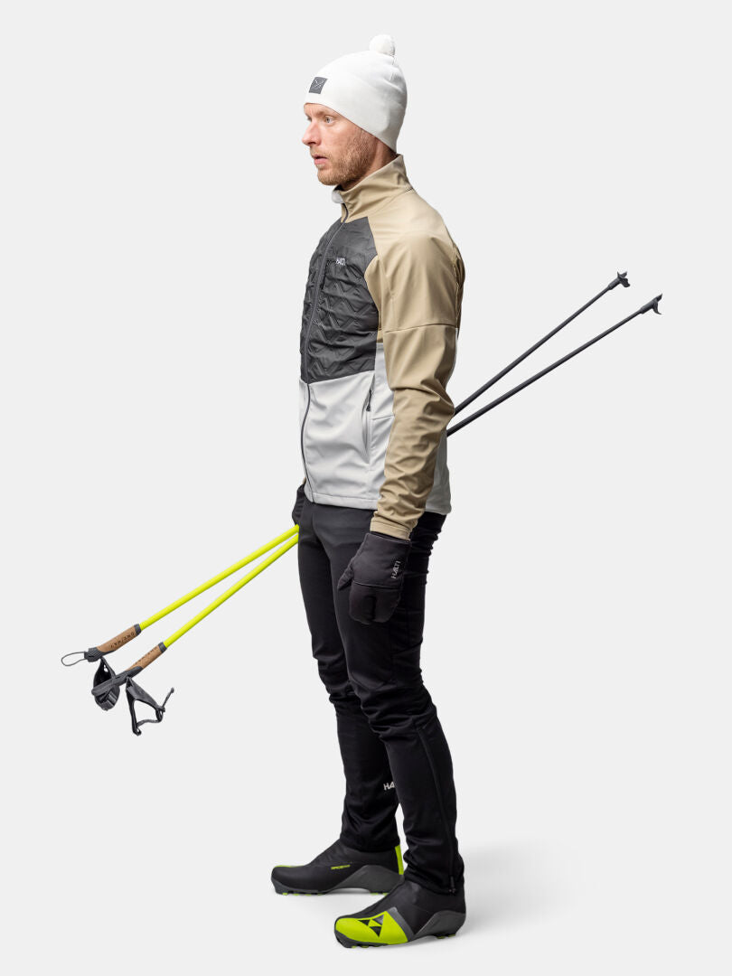 A man in the Halti Framover Hybrid XCT Jacket stands with ski poles, facing sideways against a plain light background.