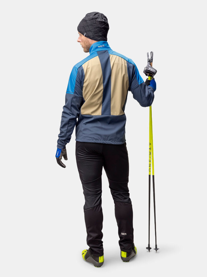 A man in a Halti Framover XCT Jacket holds ski poles and flashes a peace sign, wearing winter sportswear.