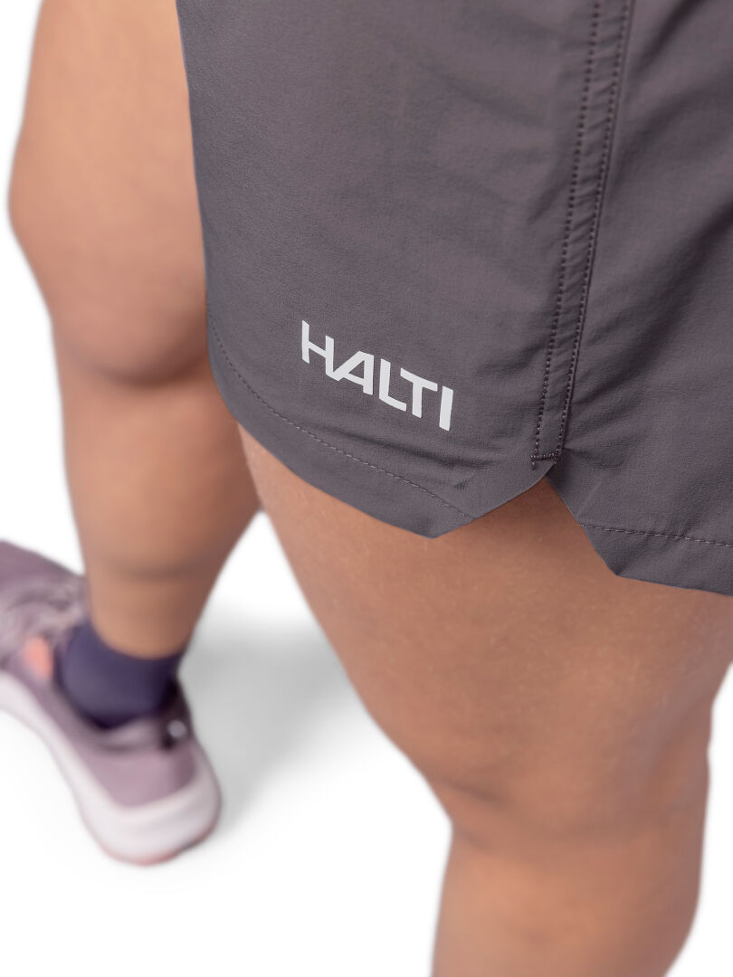 Close-up of a person wearing Halti Uurto Shorts Women's in gray with pink athletic shoes, shown from the thigh down.