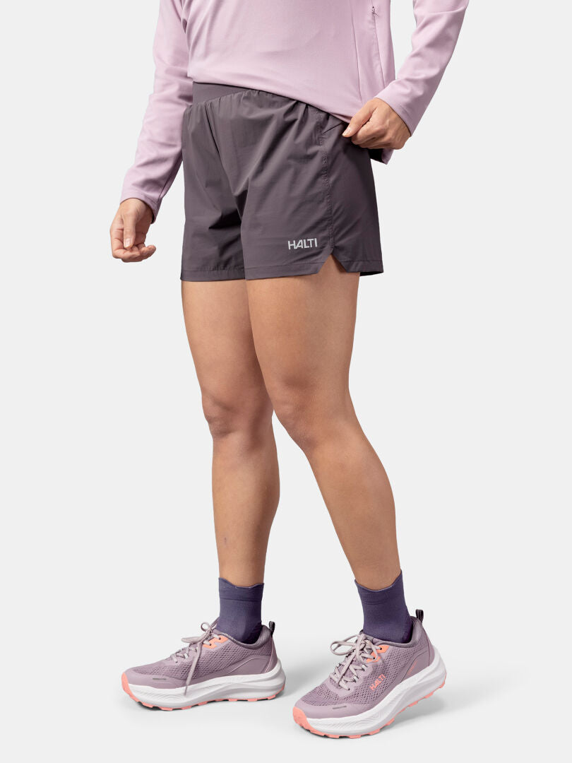 Person wears a lavender long-sleeve, Halti Uurto Shorts Women's, purple socks, and sneakers on white backdrop.